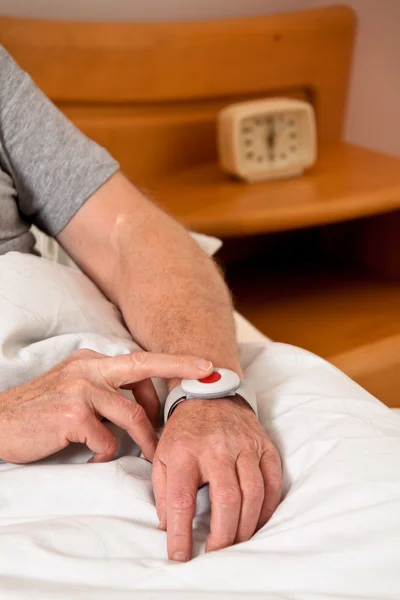 Senior rufhilfe with emergency phone in bed — Stock Photo, Image