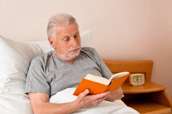 Старший в доме престарелых, чтобы прочитать книгу в постели — стоковое фото