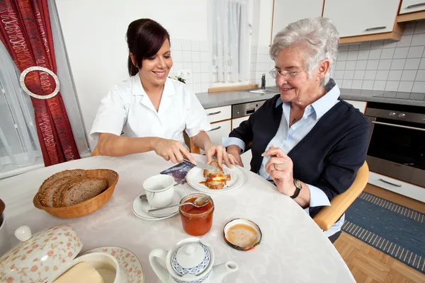 Enfermeira ajuda mulher idosa no café da manhã — Fotografia de Stock