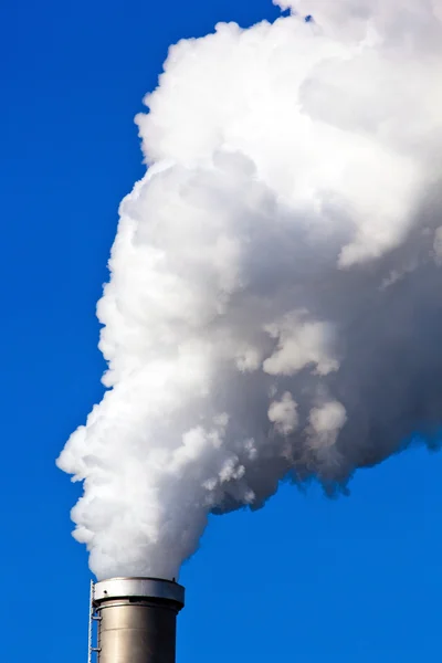 Las chimeneas humeantes de una fábrica contra un cielo azul . —  Fotos de Stock