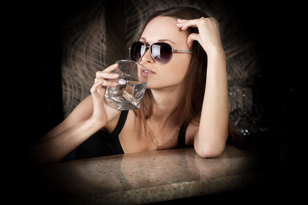 Sensual brunette girl in sun glasses with a glass of vodka