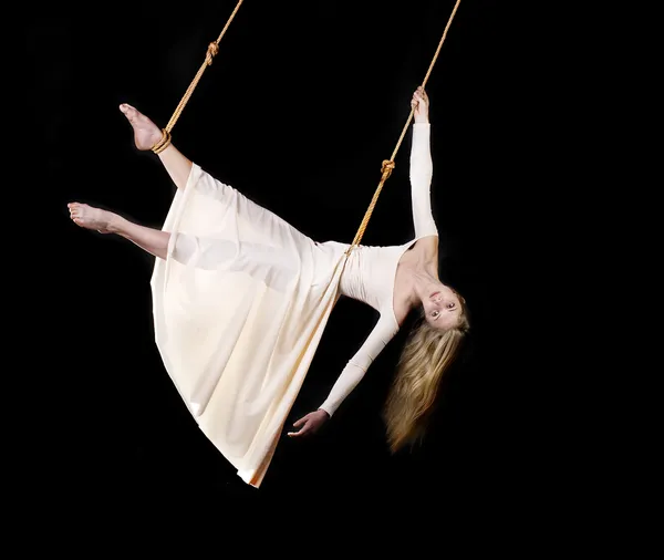 Молода жінка гімнастка в білій сукні на мотузці на чорному тлі — стокове фото