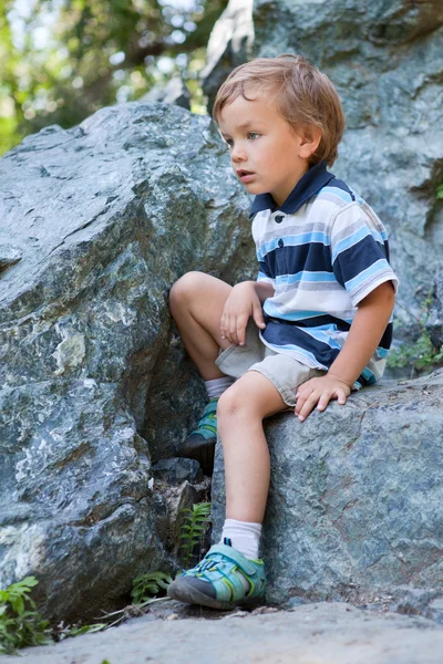 Triste menino sentado na rocha . — Fotografia de Stock