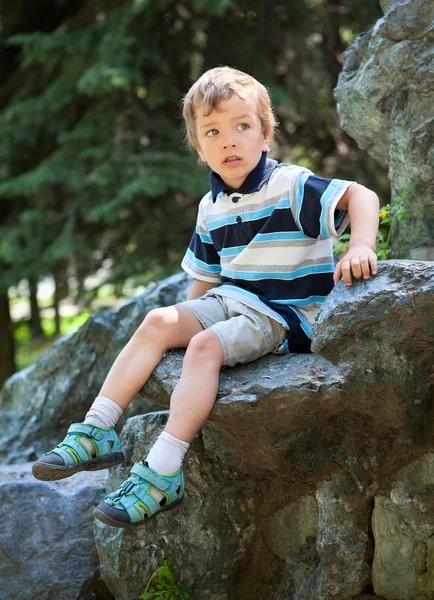 Triste menino sentado na rocha . — Fotografia de Stock