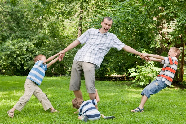 Far och tre söner spelar i parken. — Stockfoto
