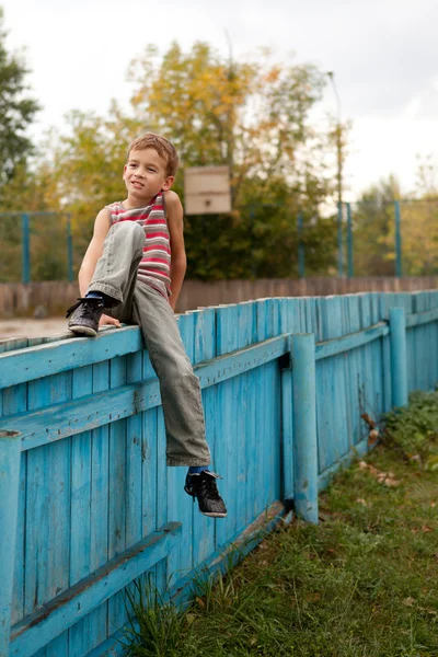 Fröhlicher Junge sitzt auf dem Zaun. — Stockfoto