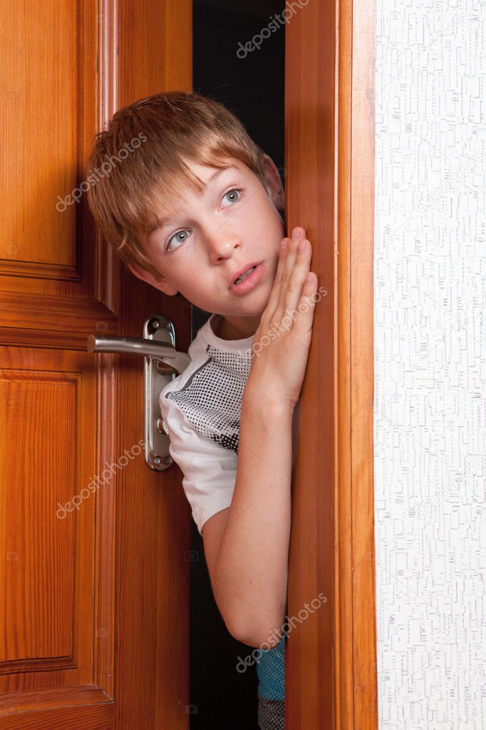 Surprised boy peeks from behind door