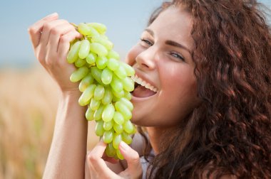 Perfect woman eating grapes in wheat field. Picnic. clipart