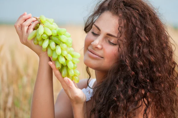 完璧な女性は麦畑のブドウを食べるします。ピクニック. — ストック写真
