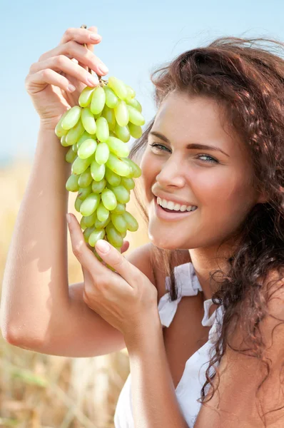 完璧な女性は麦畑のブドウを食べるします。ピクニック. — ストック写真