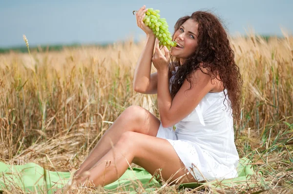 Perfekte Frau beim Traubenessen im Weizenfeld. Picknick. — Stockfoto