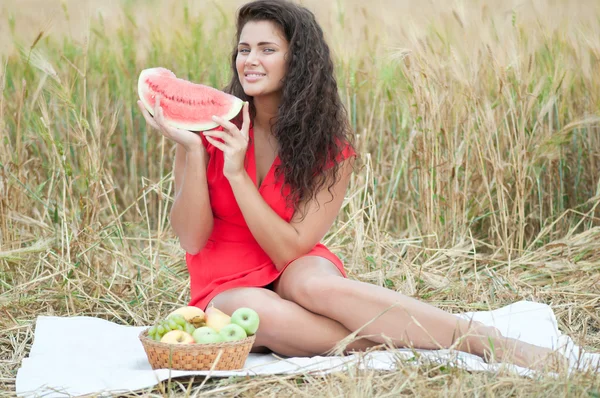 Kobieta w polu pszenicy jedzenie arbuza. piknik. — Zdjęcie stockowe