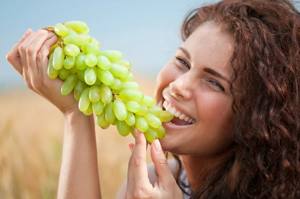 Uma mulher perfeita a comer uvas no campo de trigo. Piquenique . — Fotografia de Stock