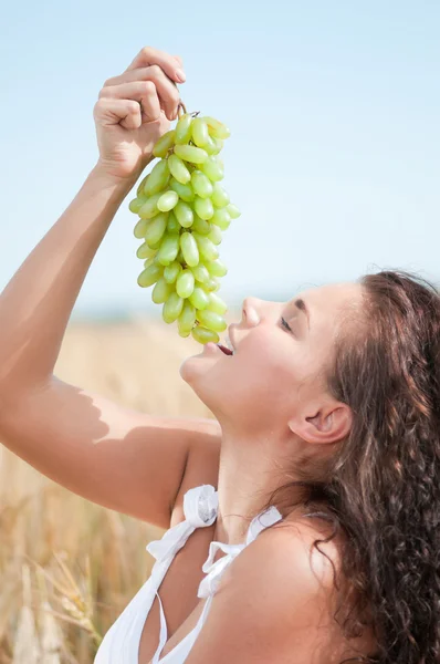 Uma mulher perfeita a comer uvas no campo de trigo. Piquenique . — Fotografia de Stock