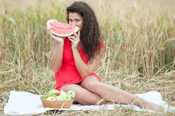 Kobieta w polu pszenicy jedzenie arbuza. piknik. — Zdjęcie stockowe