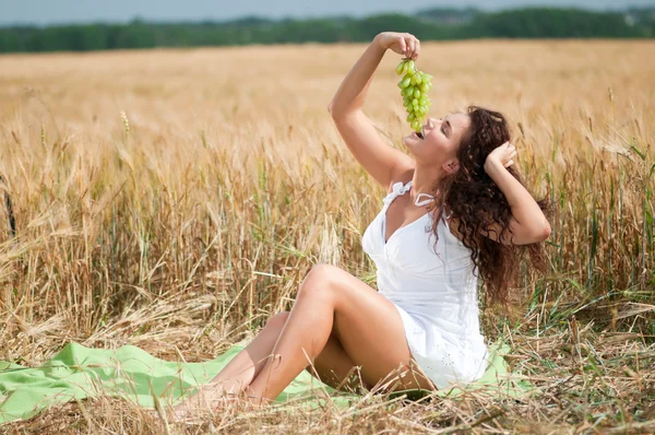 Perfecte vrouw druiven eten in tarweveld. picknick. — Stockfoto