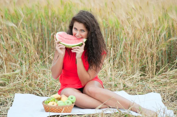 Žena v pšeničné pole jíst meloun. piknik. — Stock fotografie