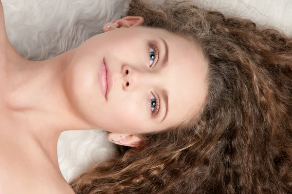 Menina com cabelo encaracolado perfeito deitado na cama de pele — Fotografia de Stock