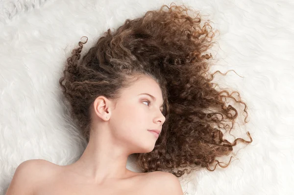 Meisje met perfecte krullend haar liggend op bont bed — Stockfoto