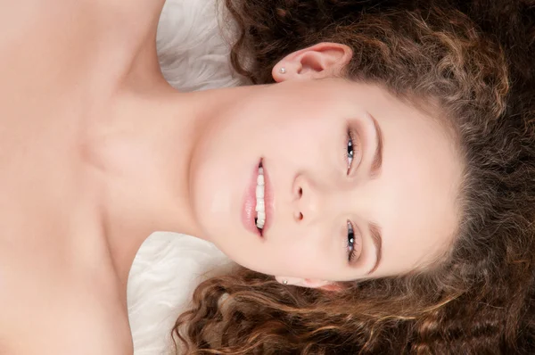 Meisje met perfecte krullend haar liggend op bont bed — Stockfoto