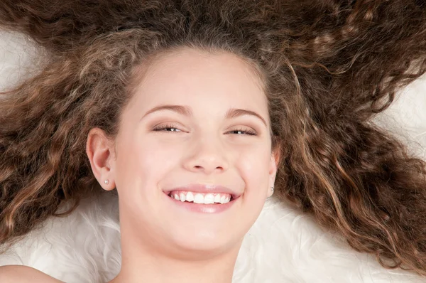 Κορίτσι με τέλεια σγουρά μαλλιά ξαπλωμένος στο κρεβάτι της γούνας — Φωτογραφία Αρχείου