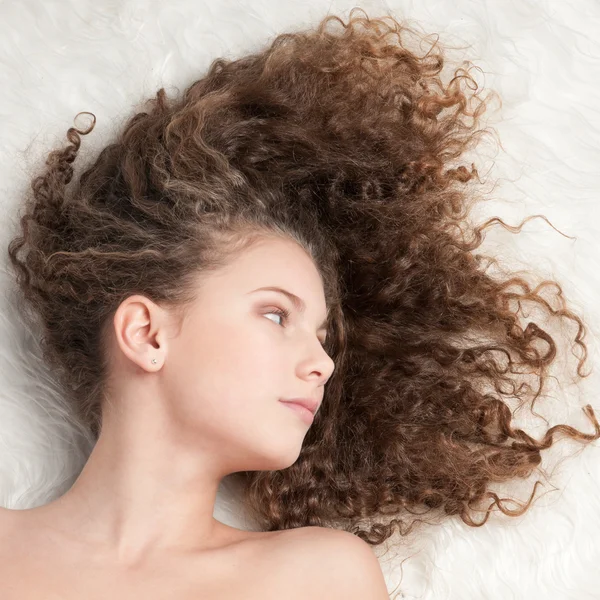 Chica con el pelo rizado perfecto acostado en la cama de piel — Foto de Stock