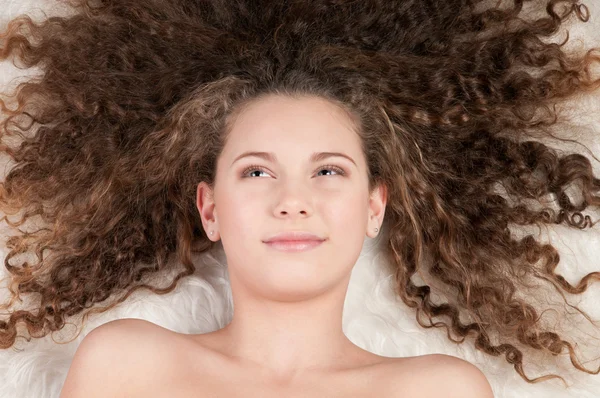 Girl with perfect curly hair lying on fur bed — Stock Photo, Image