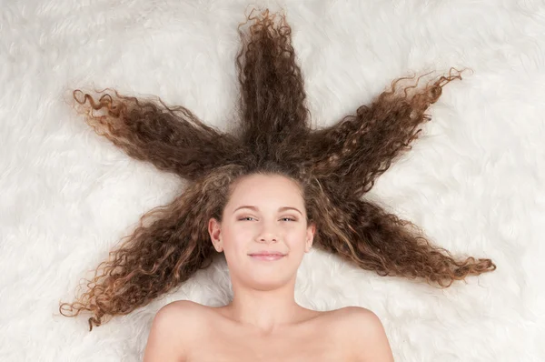 Gadis dengan rambut keriting yang sempurna berbaring di tempat tidur bulu — Stok Foto
