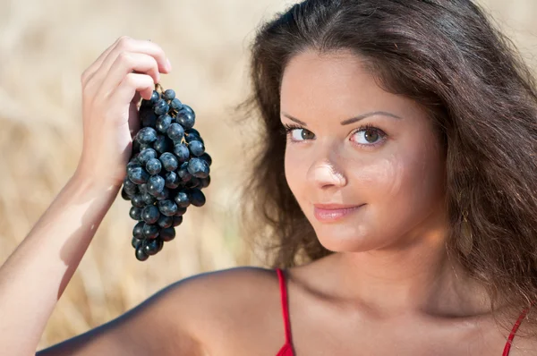 Trevlig kvinna i vete fält äta druvor. — Stockfoto