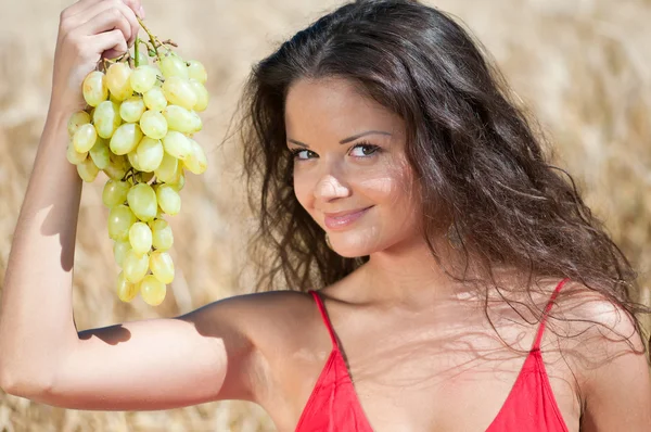 Nice woman in wheat field eating grapes. — Stock Photo, Image