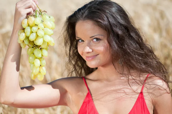 Mulher agradável no campo de trigo comendo uvas . — Fotografia de Stock