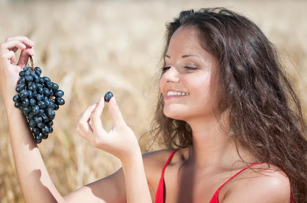Ładne kobiety w polu pszenicy, jeść winogrona. — Zdjęcie stockowe