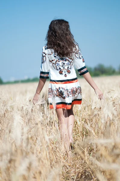 Krásná žena chodit v pšeničné pole slunečného letního dne. — Stock fotografie