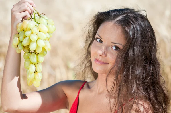 Mulher agradável no campo de trigo comendo uvas . — Fotografia de Stock