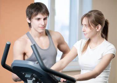 Train on machine in a gym assisted by personal instructor clipart