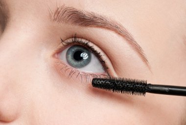 Beautiful woman applying mascara clipart