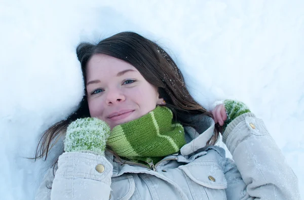 Beautiful girl in green lying in snow — Zdjęcie stockowe
