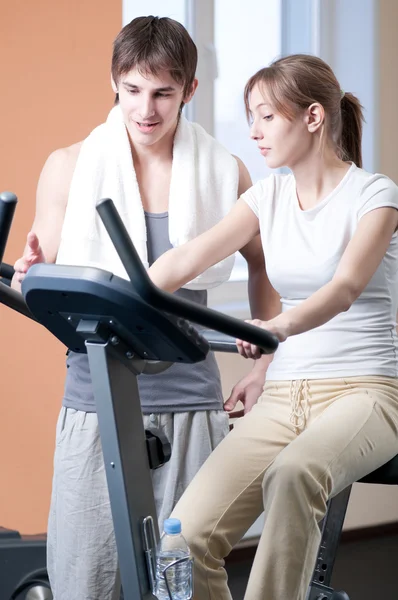 Train on machine in a gym assisted by personal instructor — Stock Photo, Image