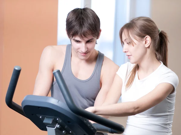 Trainen op machine in een sportschool bijgestaan door persoonlijke instructeur — Stockfoto