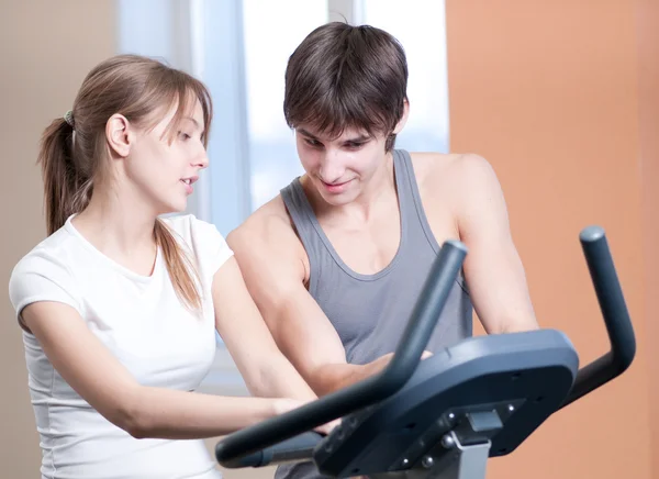 Trainen op machine in een sportschool bijgestaan door persoonlijke instructeur — Stockfoto