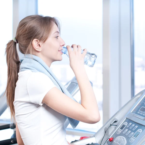 Mulher no ginásio a exercitar-se. Corra em uma máquina e beba água — Fotografia de Stock