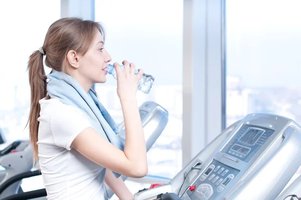 Vrouw op de sportschool uit te oefenen. op op een machine en drinken water uitvoeren — Stockfoto