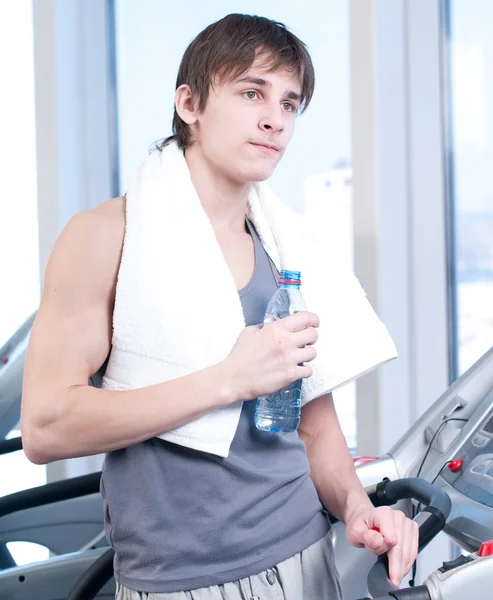 Man op de sportschool uit te oefenen. op op een machine en drinken water uitvoeren — Stockfoto