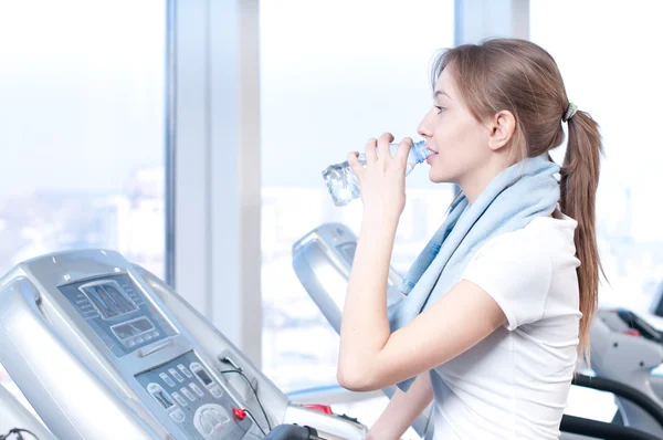 Frau im Fitnessstudio beim Training. auf einer Maschine laufen und Wasser trinken — Stockfoto