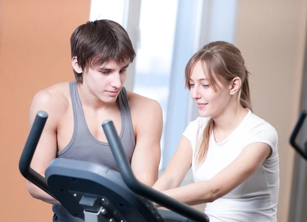 Träna på maskinen i ett gym biträdd av personlig instruktör — Stockfoto