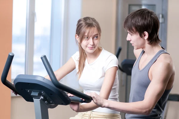 Train on machine in a gym assisted by personal instructor — Stock Photo, Image