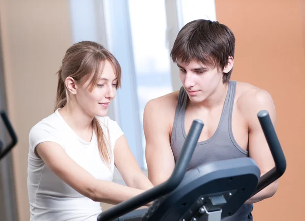 stock image Train on machine in a gym assisted by personal instructor