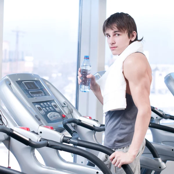 Man at the gym exercising. Run on on a machine and drink water