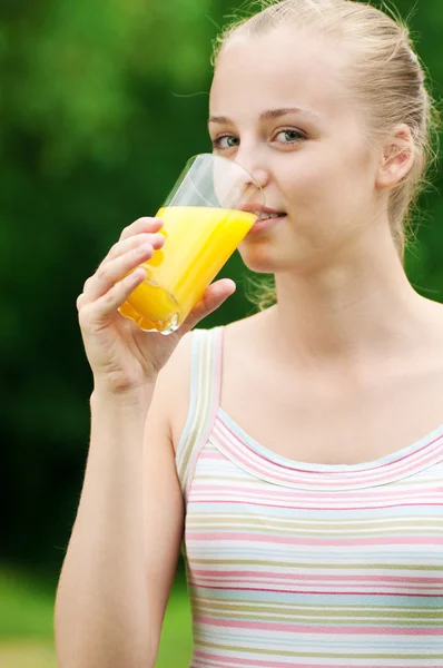 Молода жінка п'є апельсиновий сік. На відкритому повітрі — стокове фото