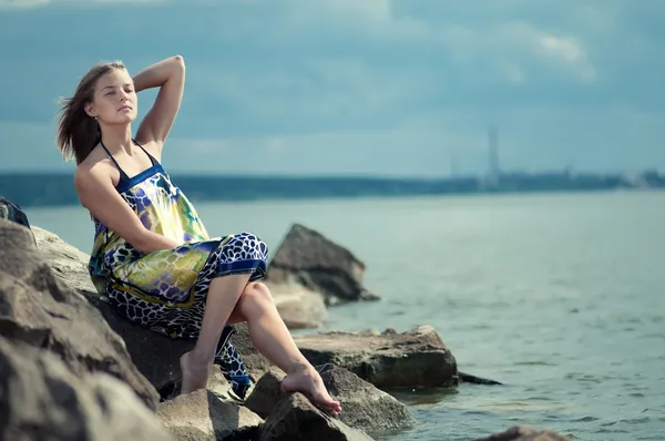 Triest vrouw in jurk zittend op rock — Stockfoto